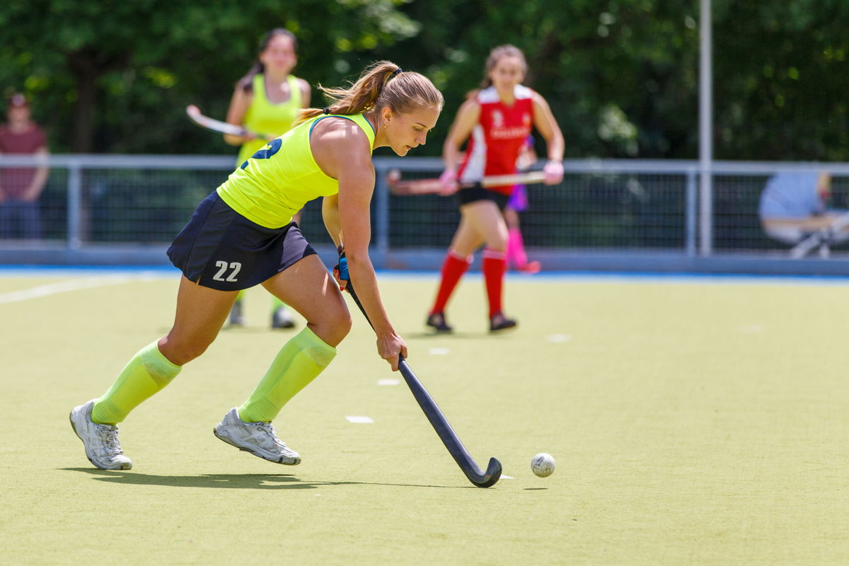 Young hockey player woman with ball in attack playing field hockey game